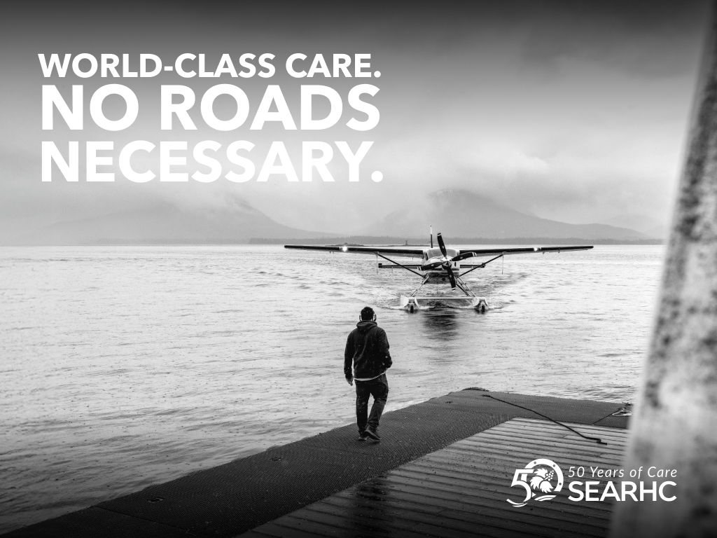 Man on dock facing seaplane in water, with mountains in background. Text: 'World-Class Care. No Roads Necessary.'
