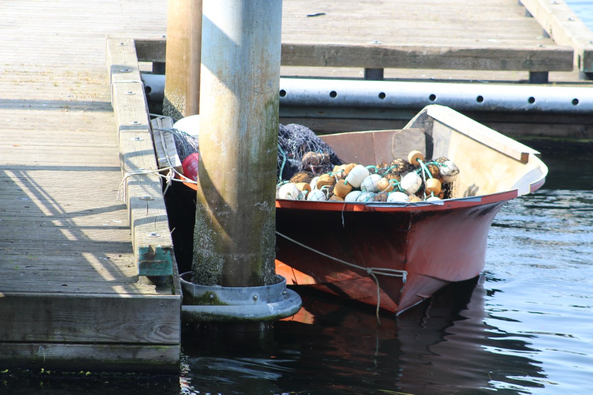 Red boat filled with fishing floats tied to dock beside a wooden pier.