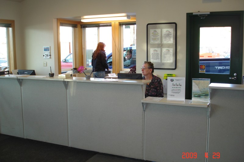 Receptionist desk with a woman sitting and another standing by the window.