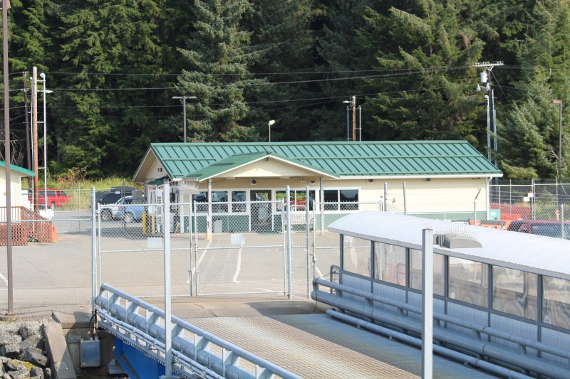 Small building with green roof behind a fenced area, surrounded by trees.