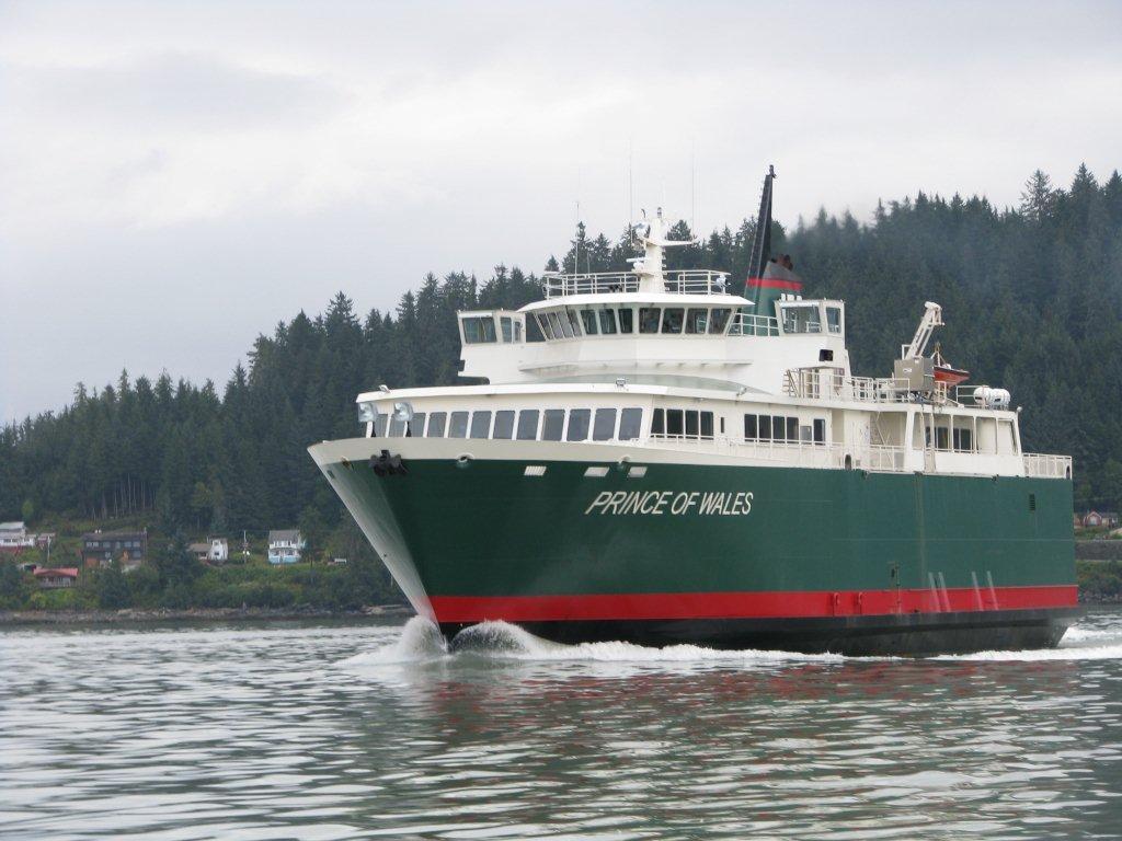 Green and white ferry ship named Prince of Wales on water, forested hills in background.